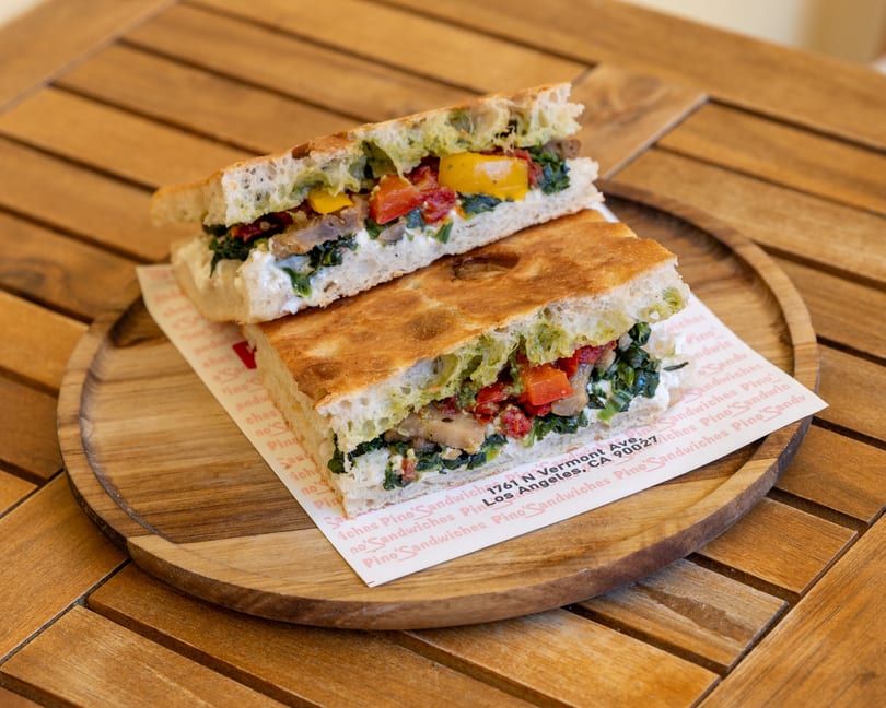 A focaccia sandwich, cut in half, filled with vegetables and cheese, on a wooden plate.