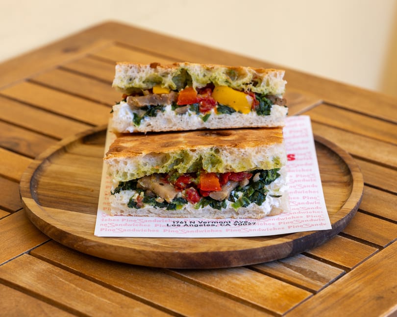 A Pino's Sandwich, cut in half, on a wooden plate, filled with vegetables and cheese.