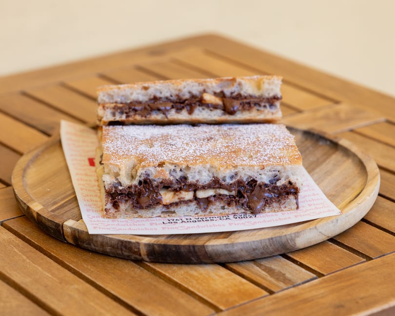 Two halves of a Nutella and banana sandwich, dusted with powdered sugar, on a wooden plate.