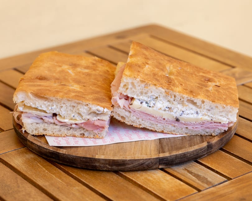 Two halves of a focaccia sandwich with ham, cheese, and ricotta on a wooden plate.