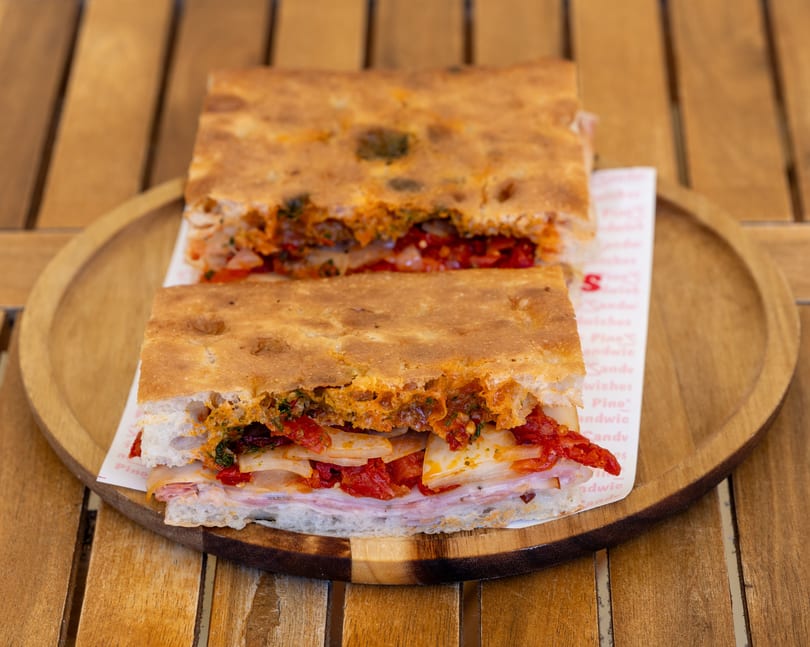 Two halves of a focaccia sandwich filled with ham, cheese, sun-dried tomatoes, and onions.
